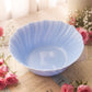 A light blue scalloped ceramic bowl placed on vintage-style printed paper with pink roses around it in a softly lit indoor setting.