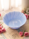 A light blue scalloped ceramic bowl placed on vintage-style printed paper with pink roses around it in a softly lit indoor setting.